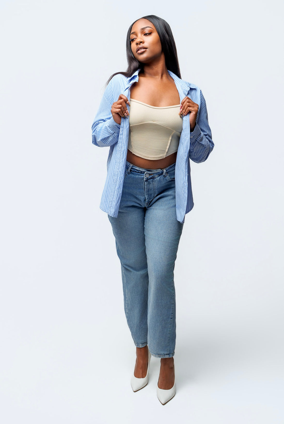 Woman wearing a light blue denim shirt, beige bralette, and jeans on a white background
