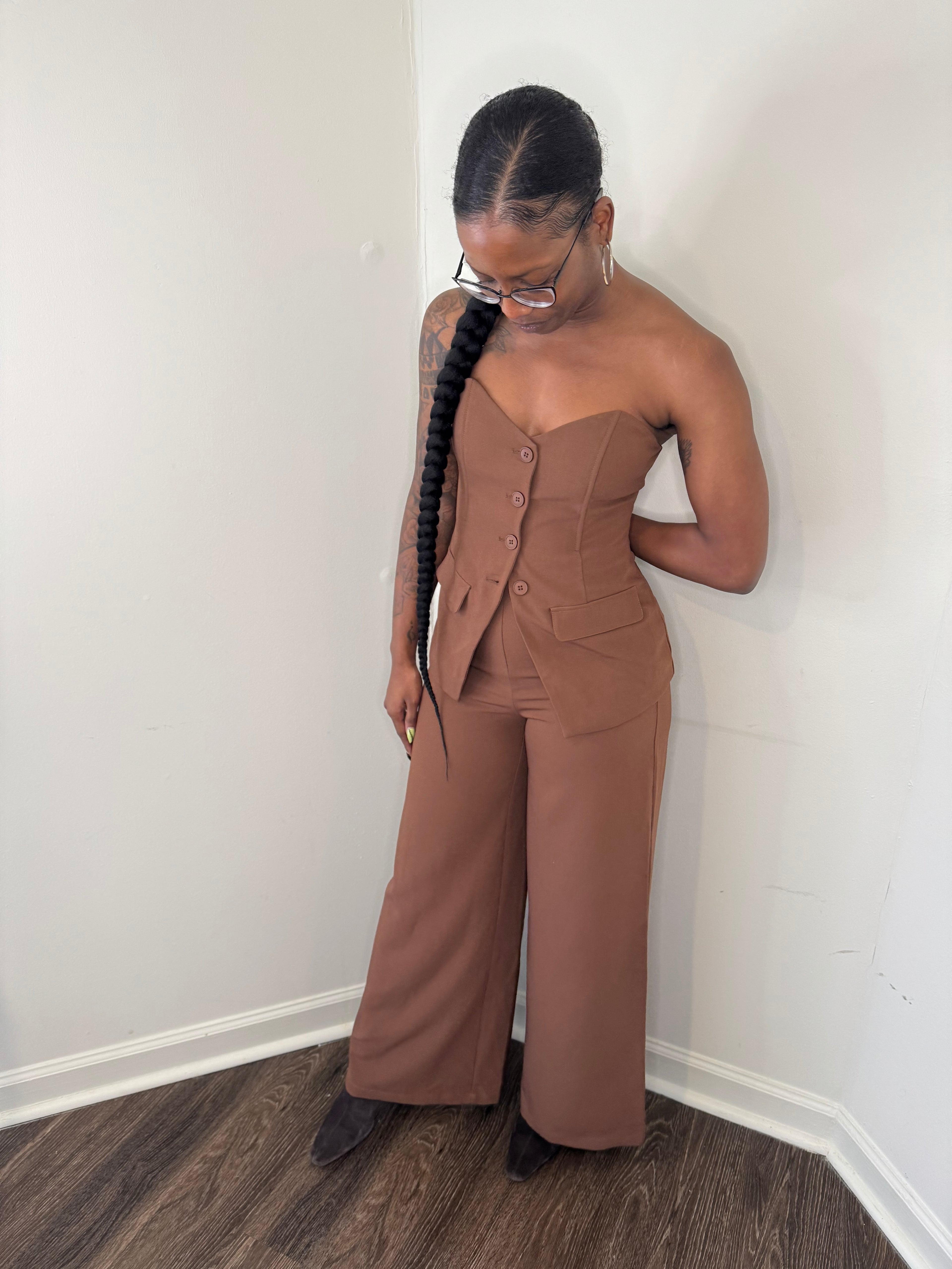 Person wearing a brown jumpsuit standing against a white wall.
