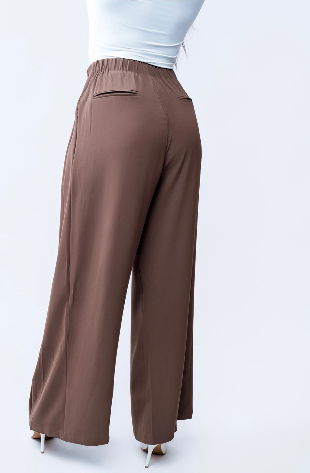 Brown wide-leg pants worn with a white top on a white background