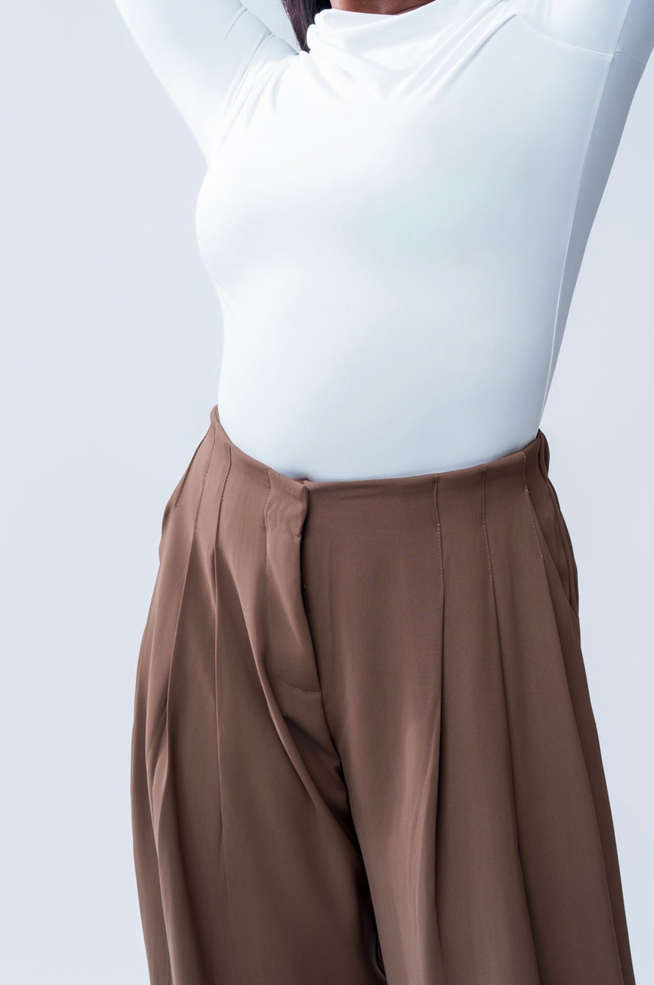 Person wearing a white top and brown pants on a light gray background