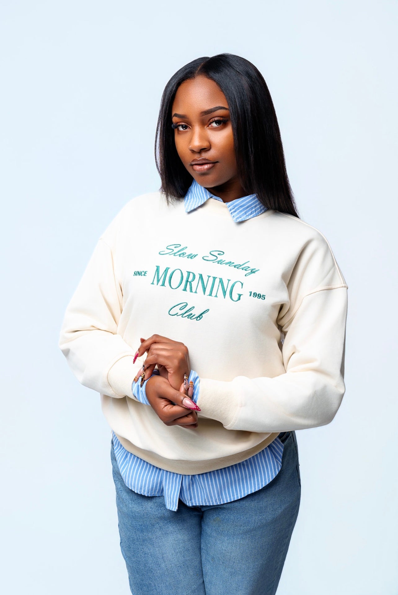 Woman wearing a cream sweatshirt with text, blue jeans, and a light blue shirt on a white background