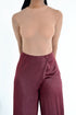Person wearing a fitted, sheer nude long-sleeve top tucked into high-waisted, wide-leg maroon satin pants, standing against a plain white background.