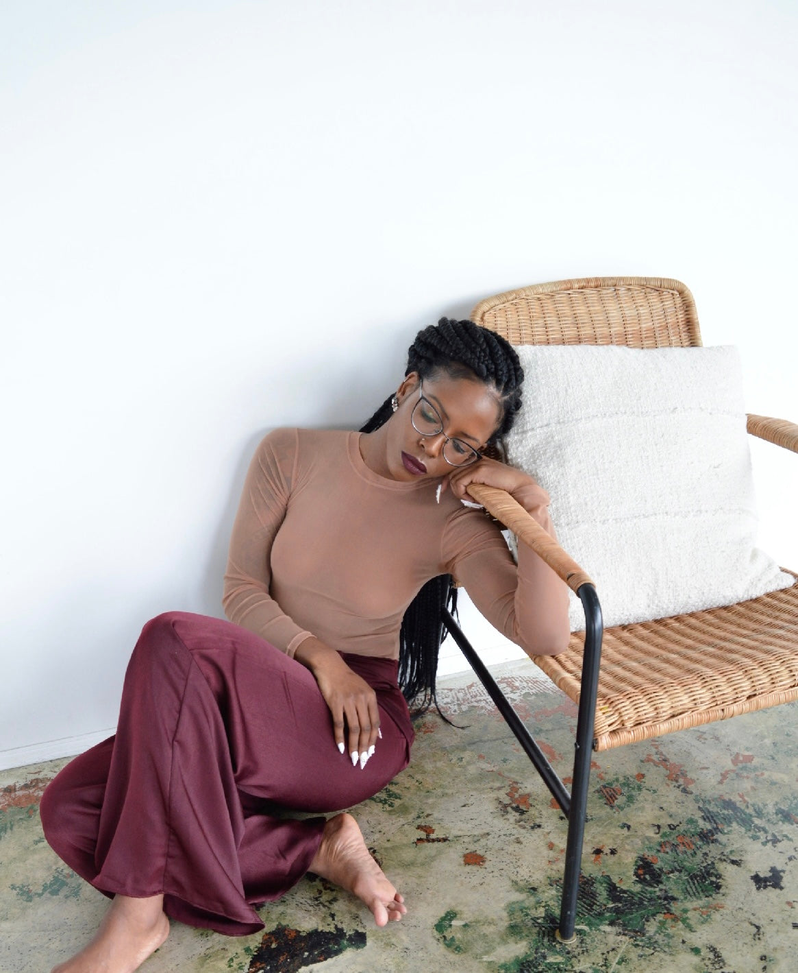 Person wearing a fitted, sheer nude long-sleeve top tucked into high-waisted, wide-leg maroon satin pants, sitting against a plain white background.