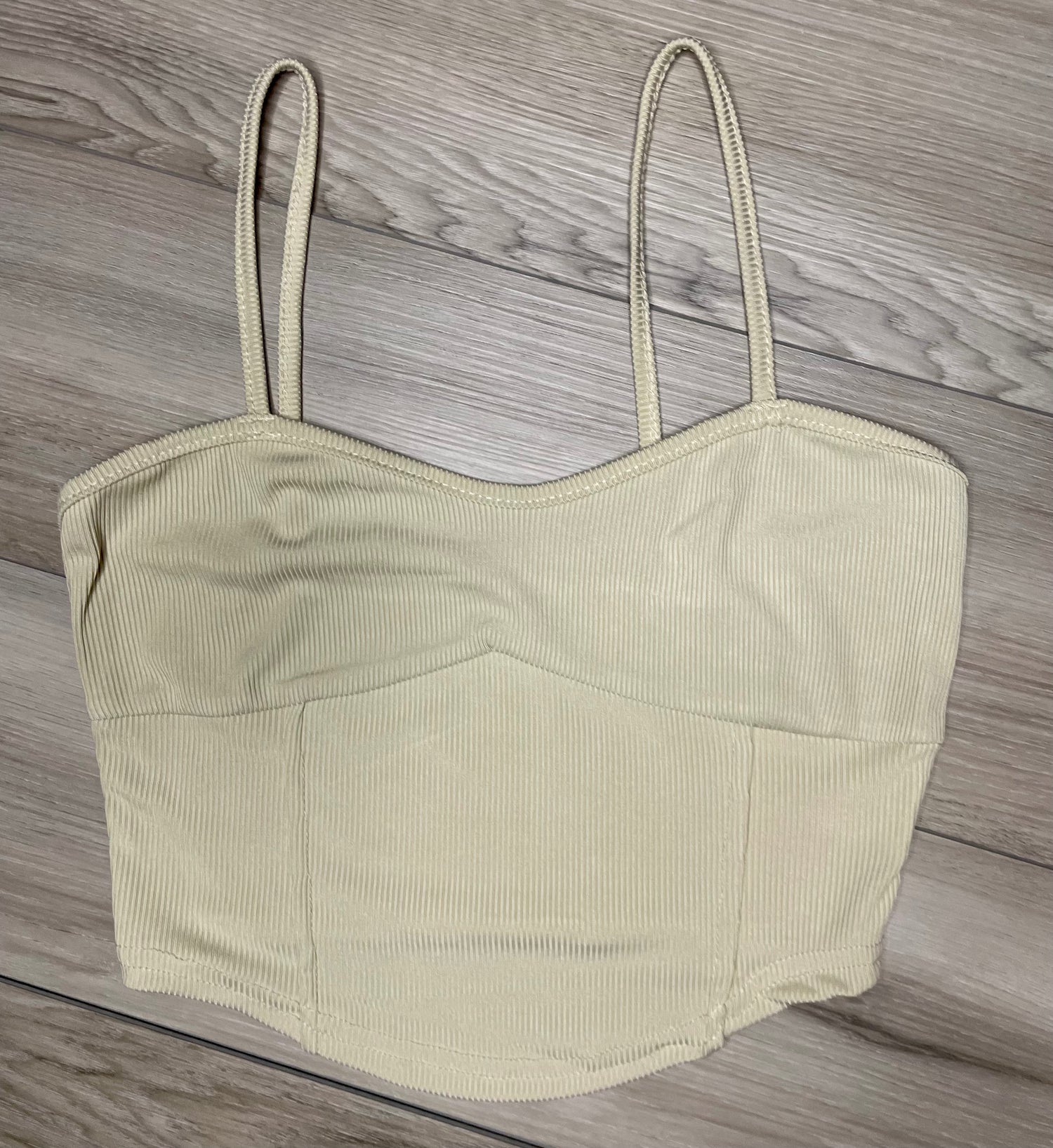 cream cropped tank top with ribbed texture  against a neutral wooden background flat. lay