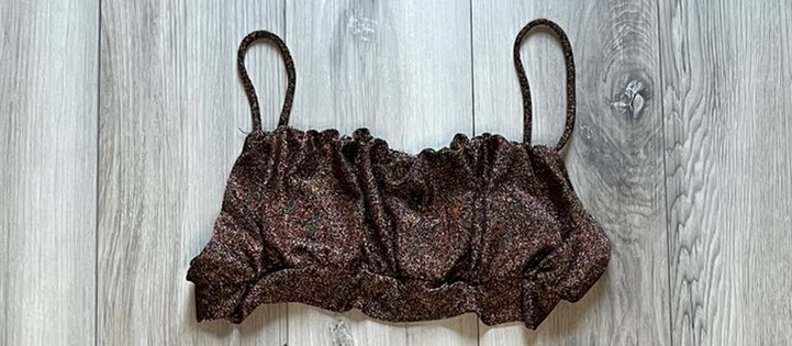 A brown, sparkly, lycra/spandex dance dress pants with a V-neck top, laid out flat on a wooden surface.