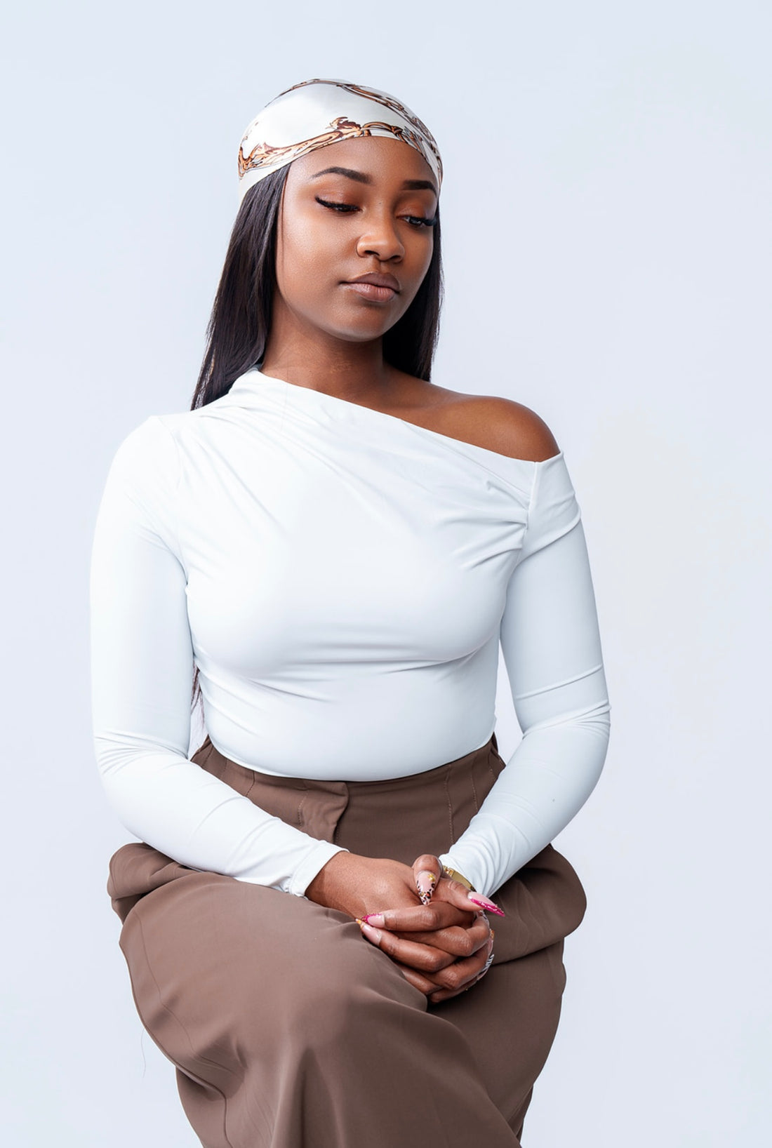 Woman wearing a white off-shoulder top and brown pants against a light gray background
