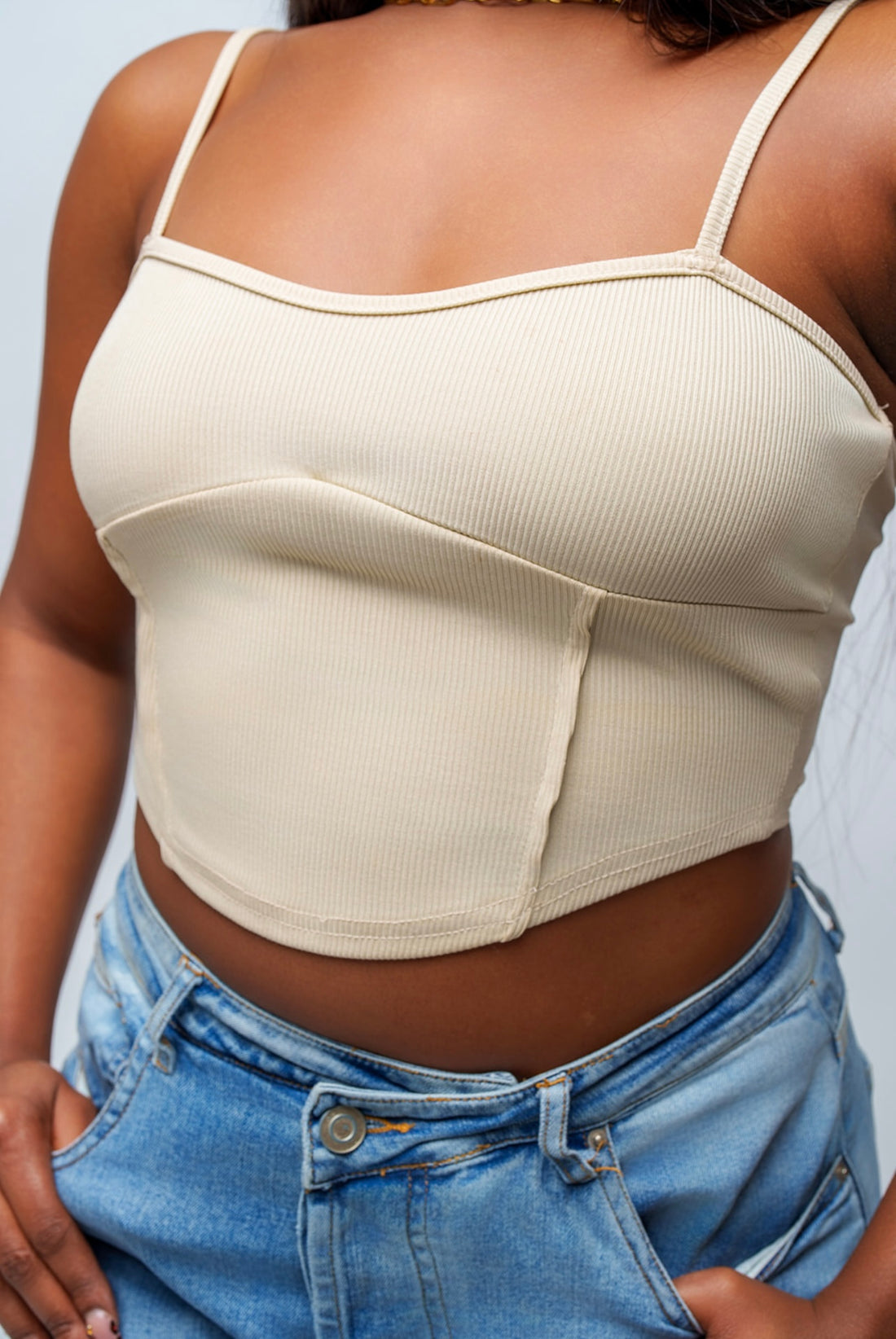 Person wearing a beige tank top and blue jeans against a neutral background