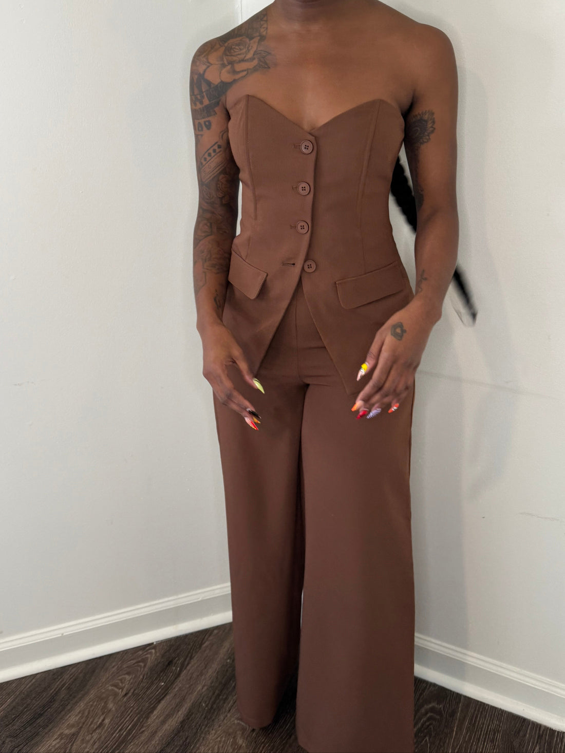 Person wearing a brown jumpsuit standing against a white wall.