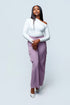 Woman wearing a white top and purple pants on a light gray background