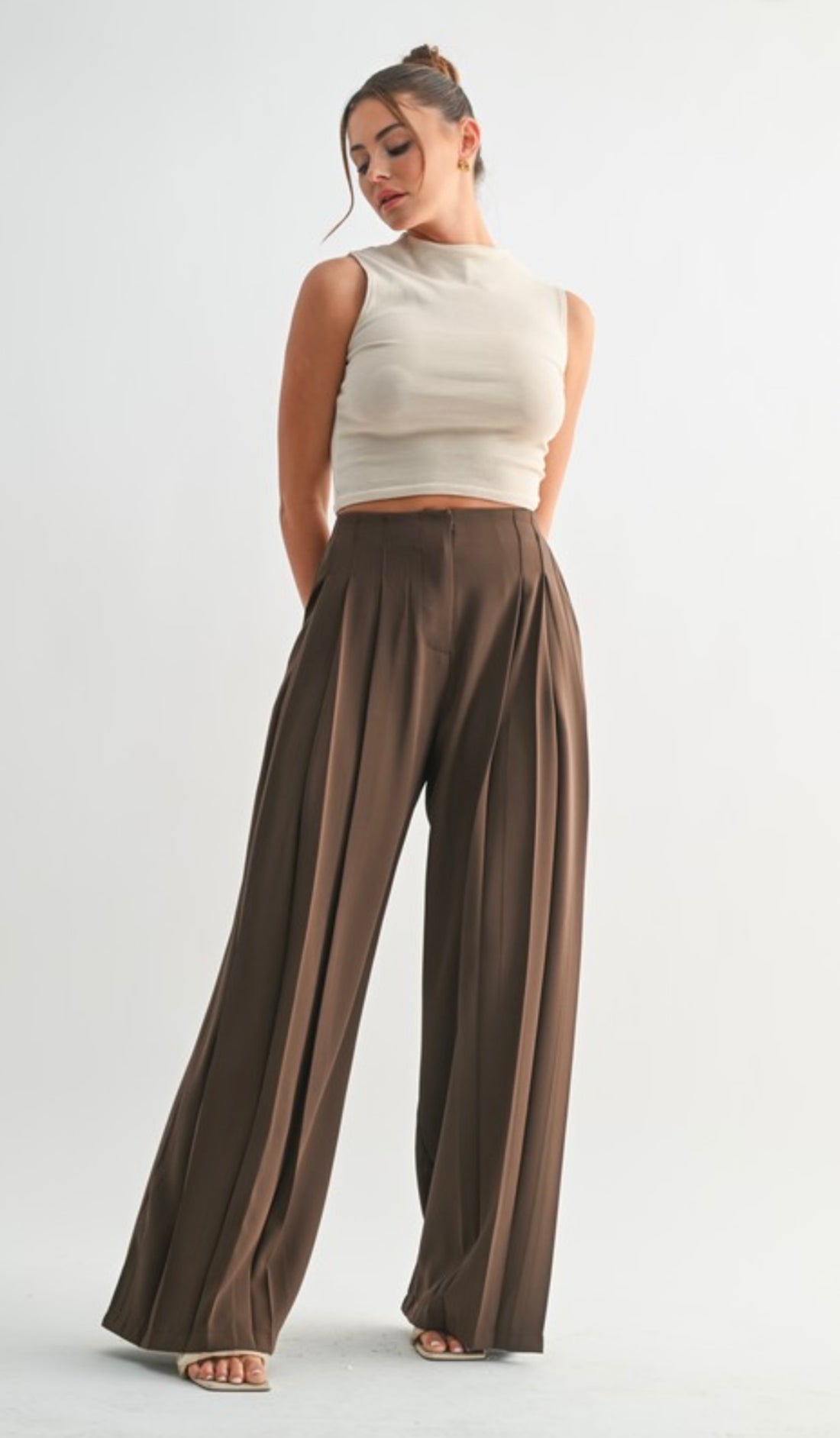 Woman wearing a white sleeveless top and brown wide-leg pants on a light gray background
