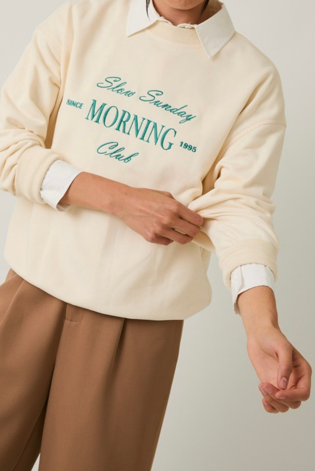 Person wearing a cream sweatshirt sweater with graphic writing on it